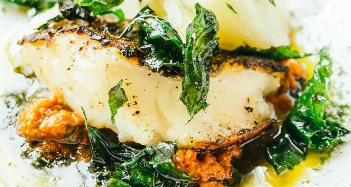 Delicioso bacalao al pil pil, con su piel dorada, acompañado de verduras frescas y una salsa vibrante.