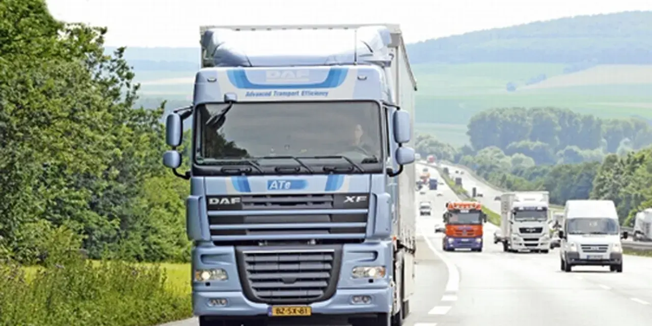Niebieska ciężarówka DAF XF 105 na autostradzie, otoczona zielenią. W tle inne pojazdy i pagórkowaty krajobraz.