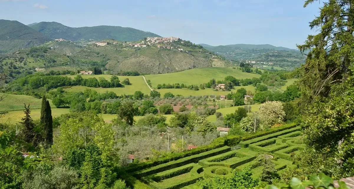 Un labirinto verdeggiante si apre su dolci colline e borghi arroccati nei Monti Sabini, un paesaggio idilliaco sotto un cielo azzurro.