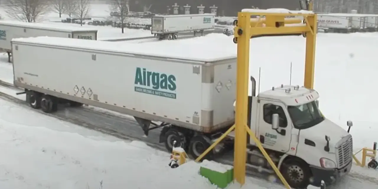 Ciężarówka z naczepą Airgas pod żółtą bramownicą w śnieżny dzień.