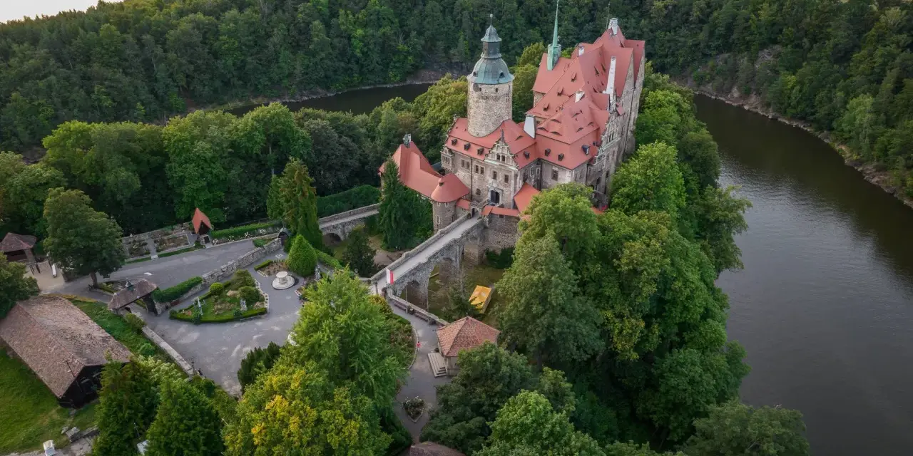 Zamek Czocha, malowniczo położony na skalistym cyplu nad rzeką, otoczony bujną zielenią.