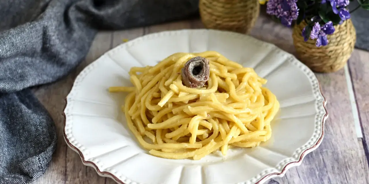 Un piatto di pasta burro e alici, condita con un tocco di sapore marino, servita su un piatto bianco decorato.