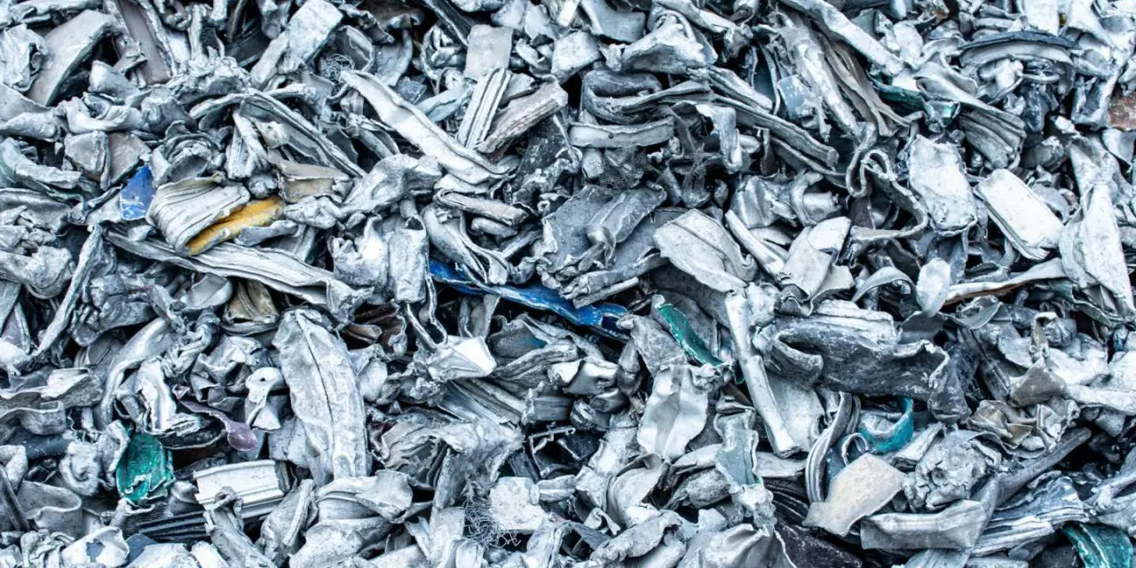 Góra poskręcanego, poszarpanego złomu metalowego, gotowego do recyklingu metalu. Widać fragmenty niebieskiego i żółtego plastiku.