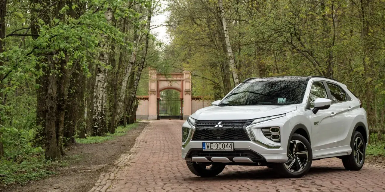 Biały Mitsubishi Eclipse Cross na tle bramy i drzew. Wiele pozytywnych mitsubishi eclipse cross opinie potwierdza jego wszechstronność.