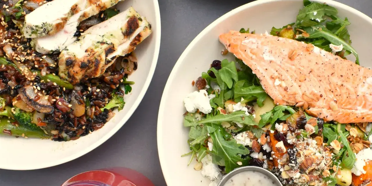 Två skålar med mat: en med grillad kyckling och vildris, en annan med lax och sallad. Perfekt för att få i sig rätt mängd protein per kilo kroppsvikt.