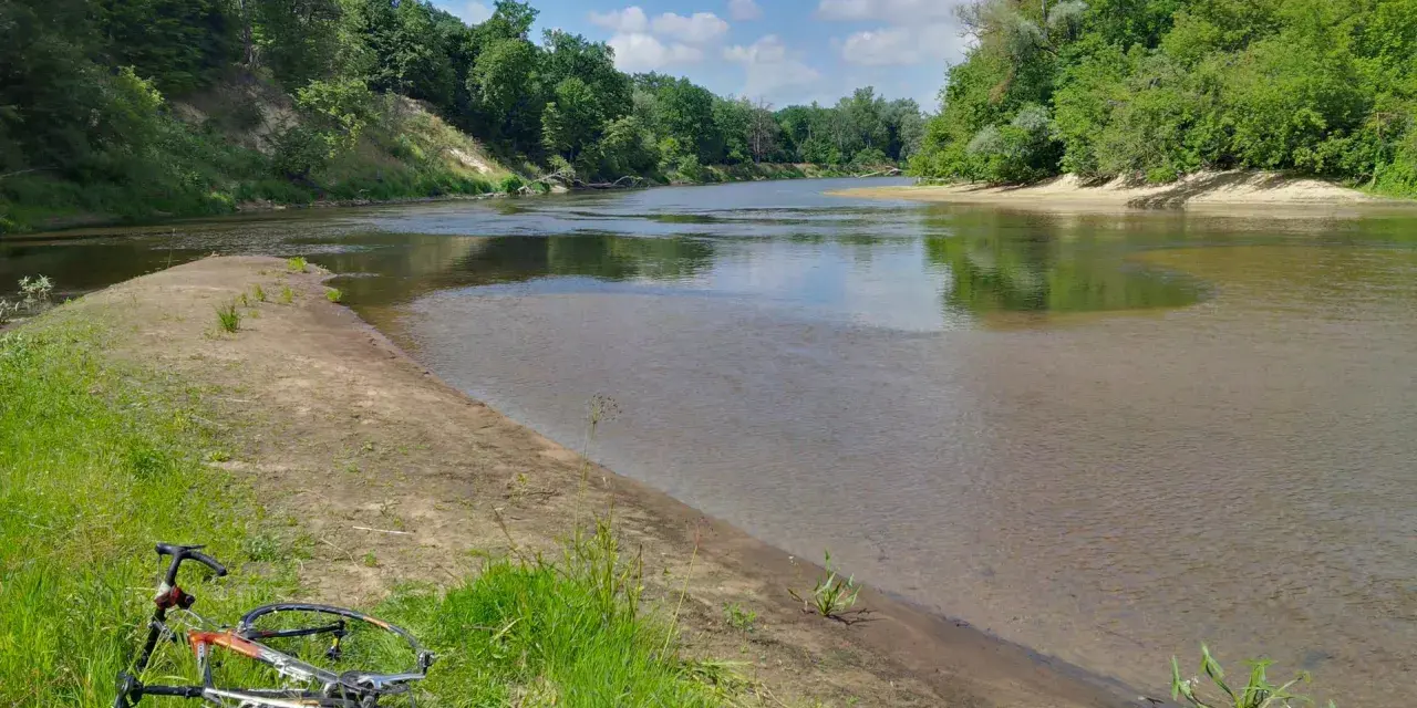 Rower leży na trawie nad rzeką, otoczoną zielenią. To malowniczy zakątek, prawdziwa szwajcaria podlaska.