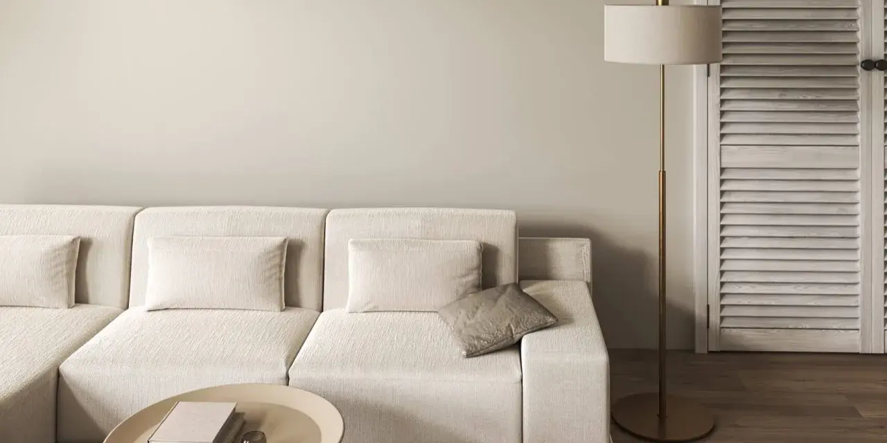 Divano modulare color tortora, tavolino ovale con libri, lampada da terra dorata e porta a soffietto in legno.