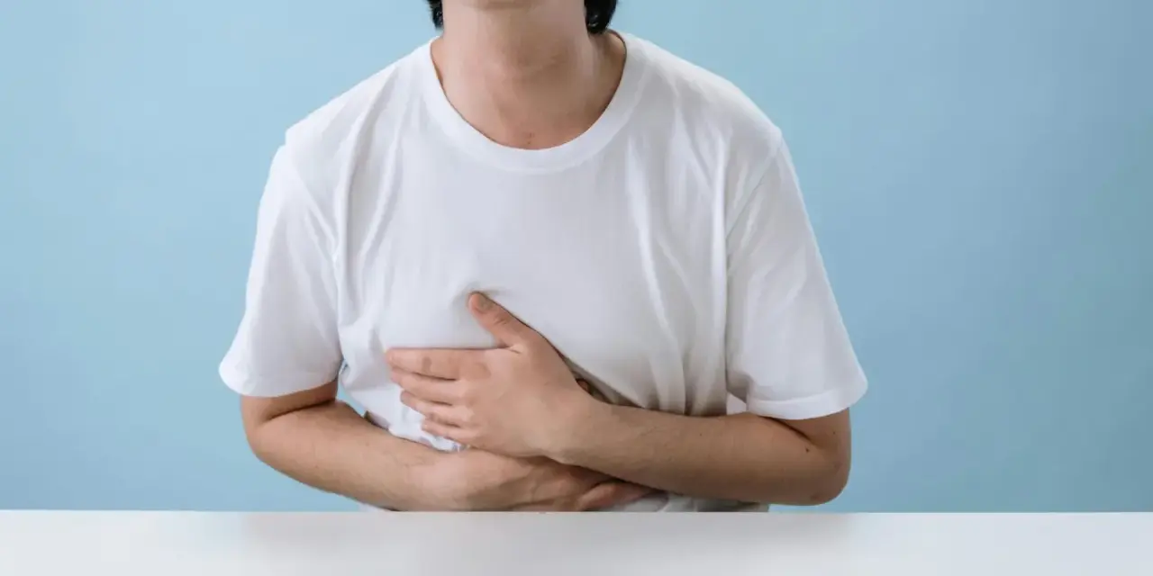 Persona con le mani sull'addome, che esprime disagio per nausea e giramenti di testa dopo allenamento.