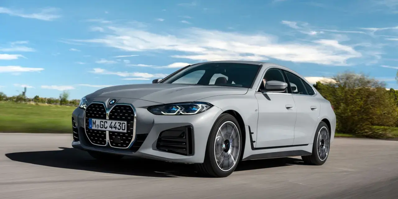 Eleganckie, szare BMW Gran Coupé sunie po drodze na tle błękitnego nieba z chmurami.