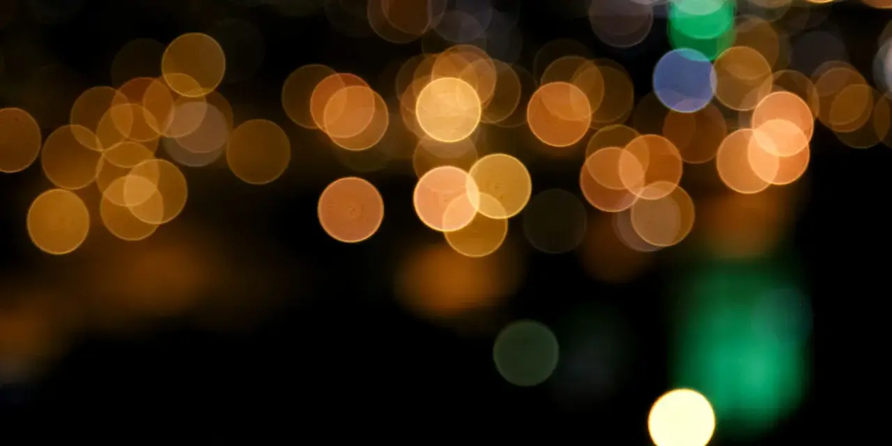 Des lumières de ville floues créent un arrière-plan bokeh chaleureux, avec des cercles dorés, verts et bleus sur fond noir.