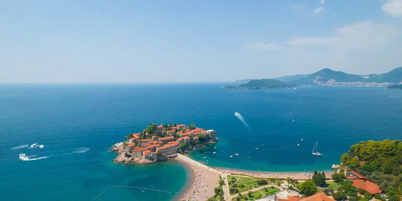Sveti Stefan, perła Czarnogóry, idealne miejsce na wycieczki. Wyspa z czerwonymi dachami, plaża, turkusowe morze i góry w tle.