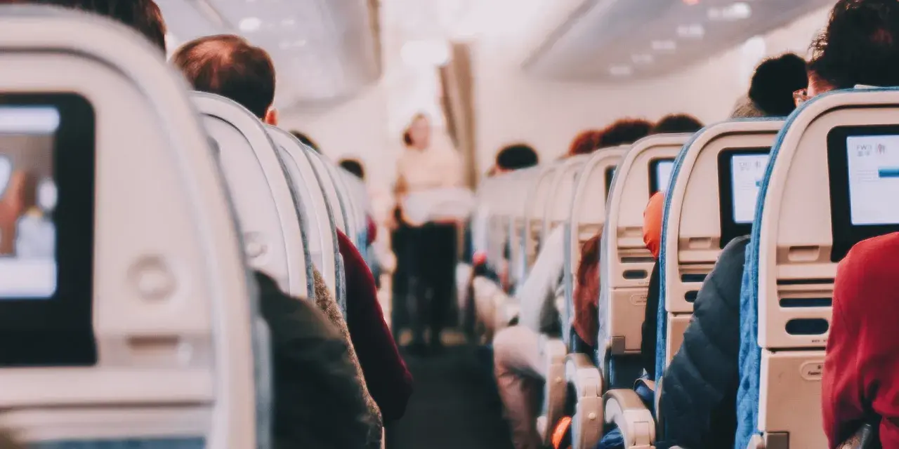 View from inside an airplane cabin, showing rows of seats with passengers and entertainment screens.
