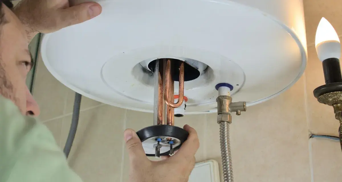 Un tecnico ripara uno scaldabagno che attacca e stacca, mostrando le resistenze in rame.