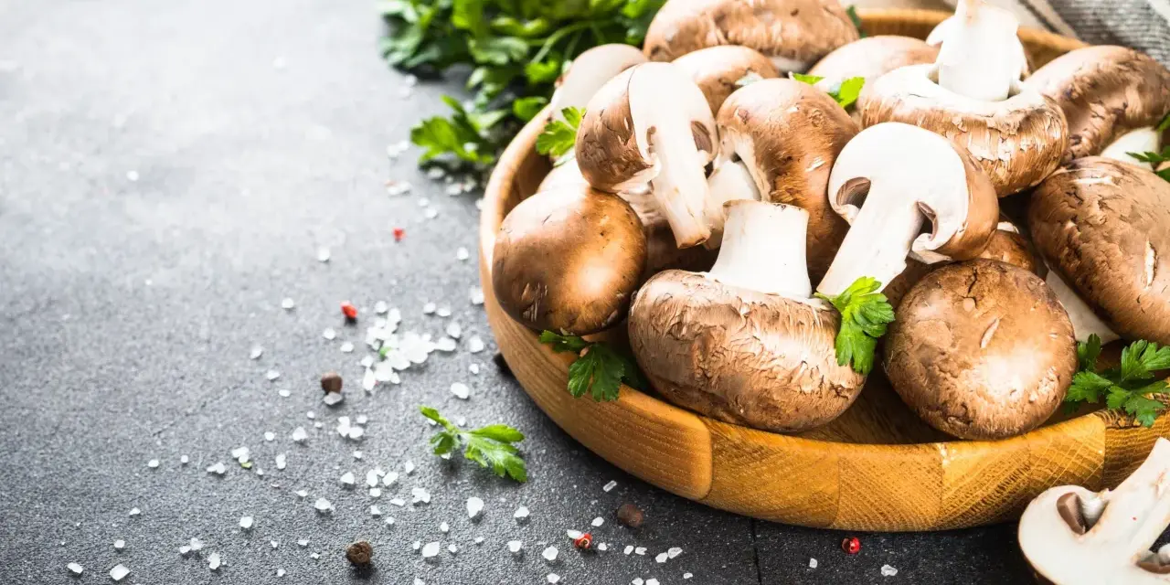 Świeże pieczarki w drewnianej misce z natką pietruszki i solą na ciemnym tle.