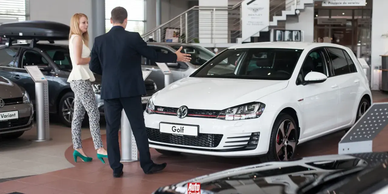 Sprzedawca prezentuje biały samochód flotowy Volkswagen Golf klientce w salonie samochodowym.
