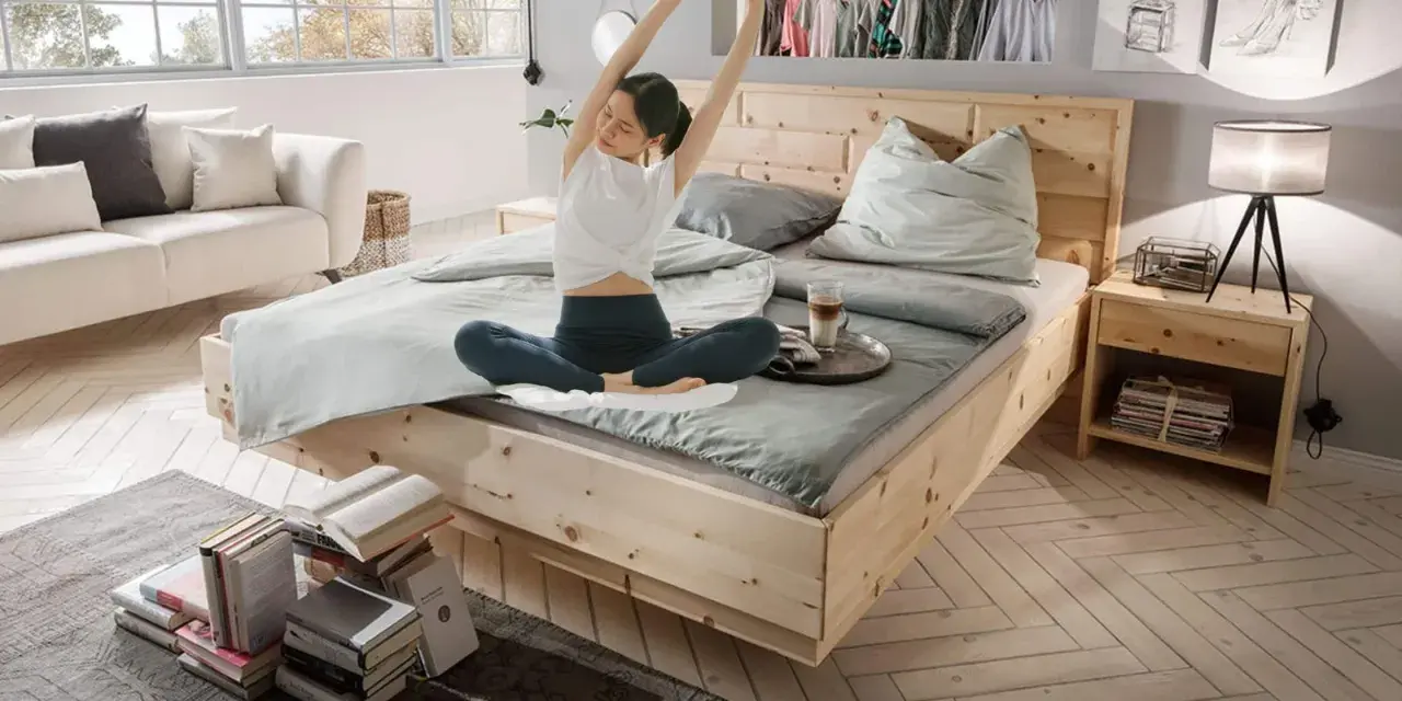 Frau dehnt sich im hellen Schlafzimmer. Ein gemütliches Bett, ein Sofa und Bücher laden zum Entspannen ein. Perfekt, um das Schlafzimmer einzurichten.