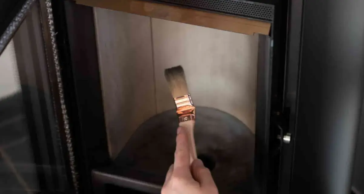 Mano con pennello per pulire il vetro della stufa bruciato.