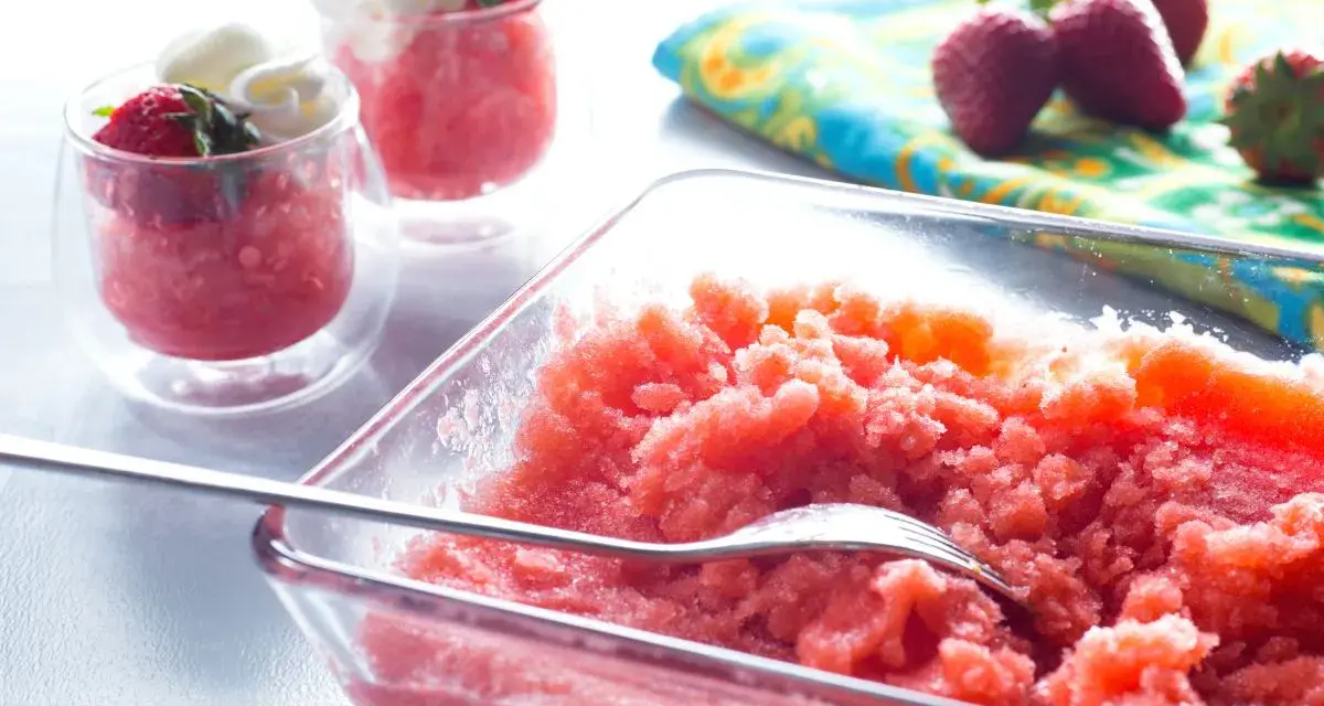 Erfrischende Erdbeer Granita in einer Glasschale, garniert mit frischen Erdbeeren und Sahne in kleinen Gläsern.