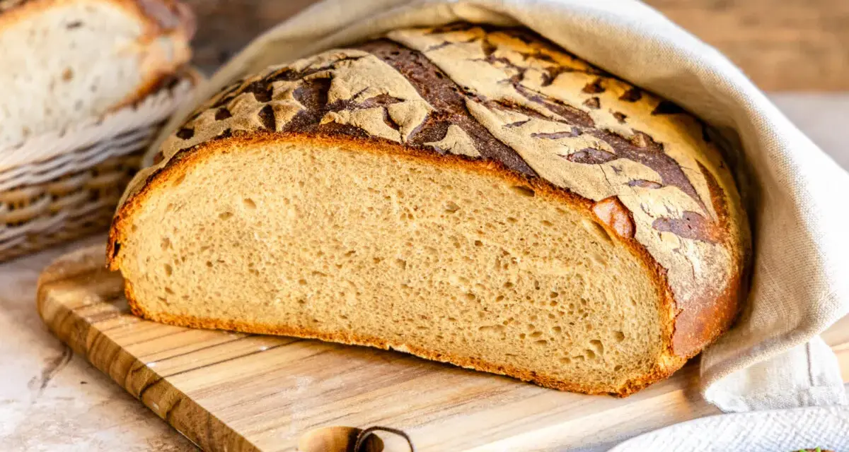 Frisches Brot mit knuspriger Kruste, bereit, mit Wasser bestrichen zu werden. Daneben ein Korb mit weiteren Brotscheiben.