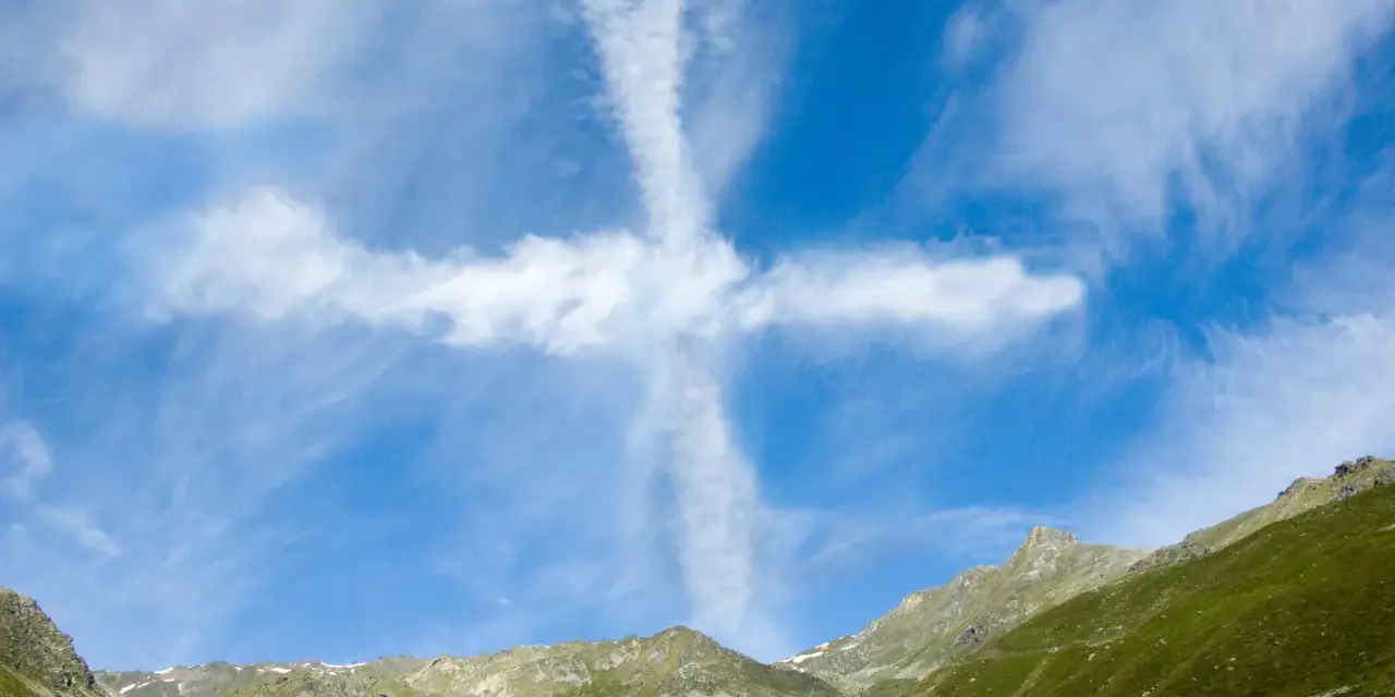 Ein Kreuz aus Wolken am blauen Himmel über grünen Bergen. Man könnte sagen, ihr werdet Zeichen am Himmel sehen.