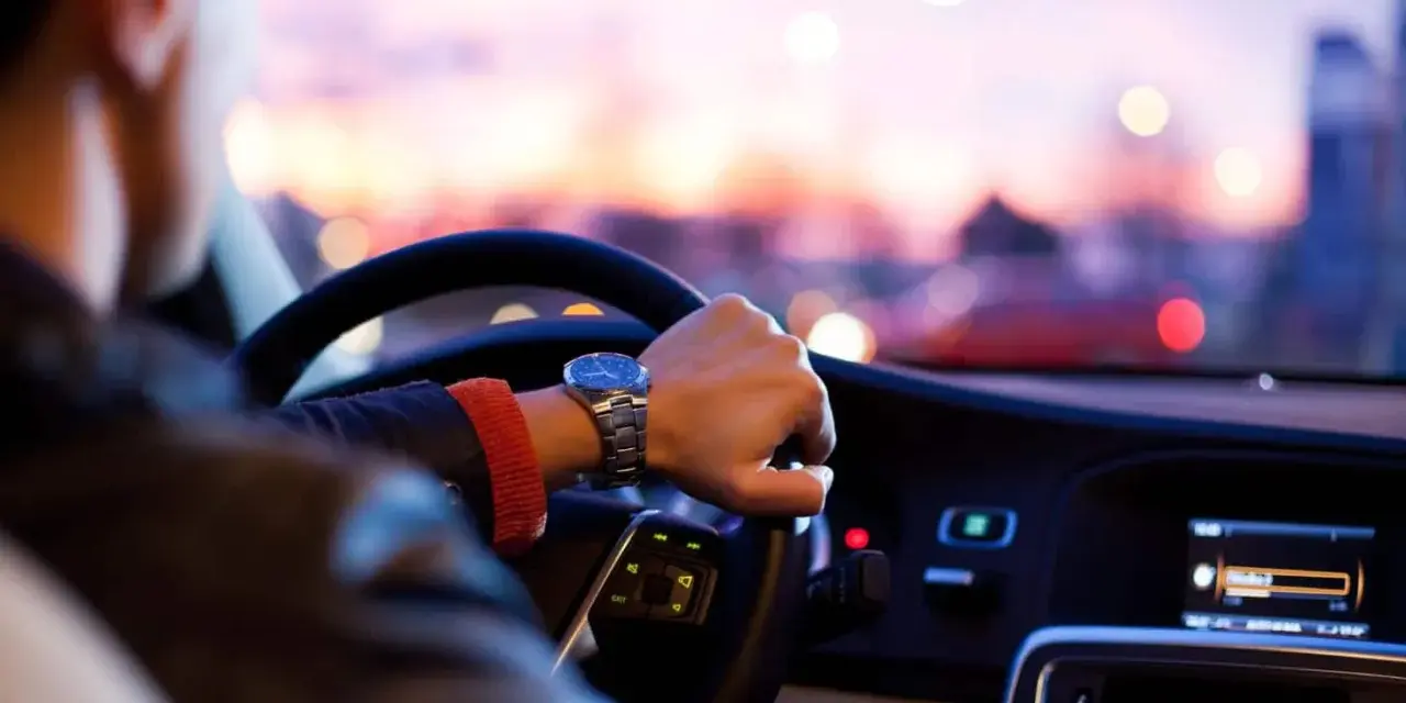 Uomo al volante, con un orologio al polso, pronto per un nuovo uber lavoro al tramonto.