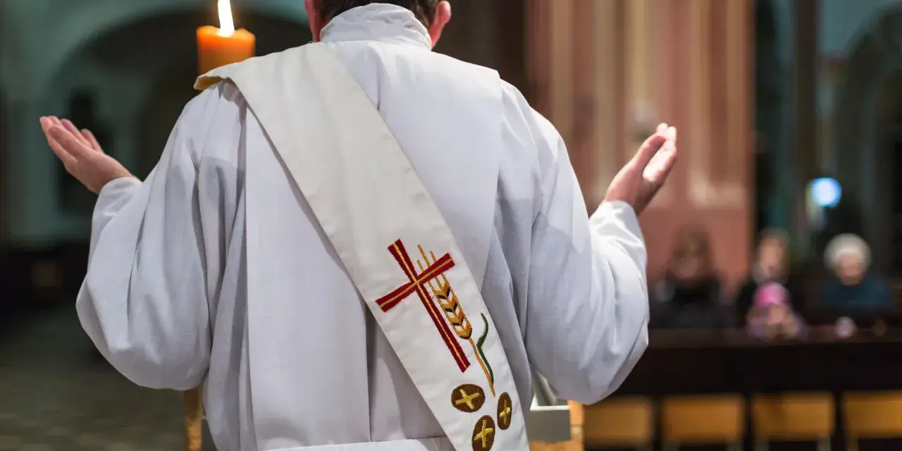 Ksiądz w białej szacie z krzyżem i kłosem na stułę, z rękami wzniesionymi w geście modlitwy, tworzy atmosferę religijnej suspensy.
