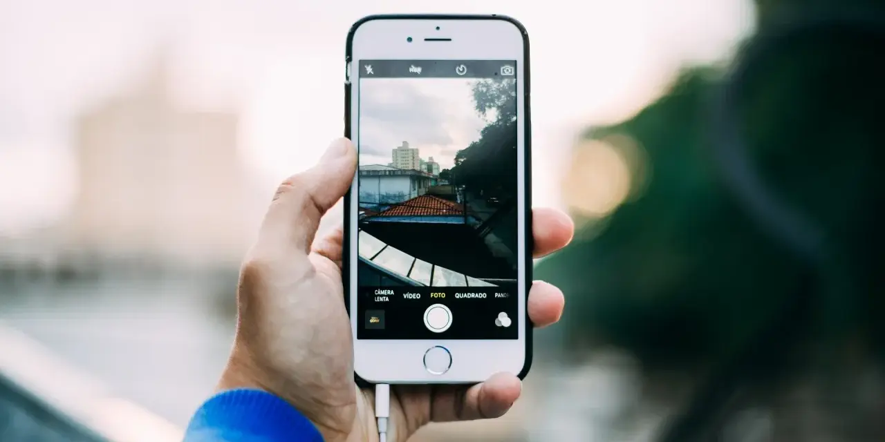 Dłoń trzyma iPhone'a, pokazując ekran z widokiem miasta. Dowiedz się, jak robic zdjecia iphonem, by uchwycić takie ujęcia.