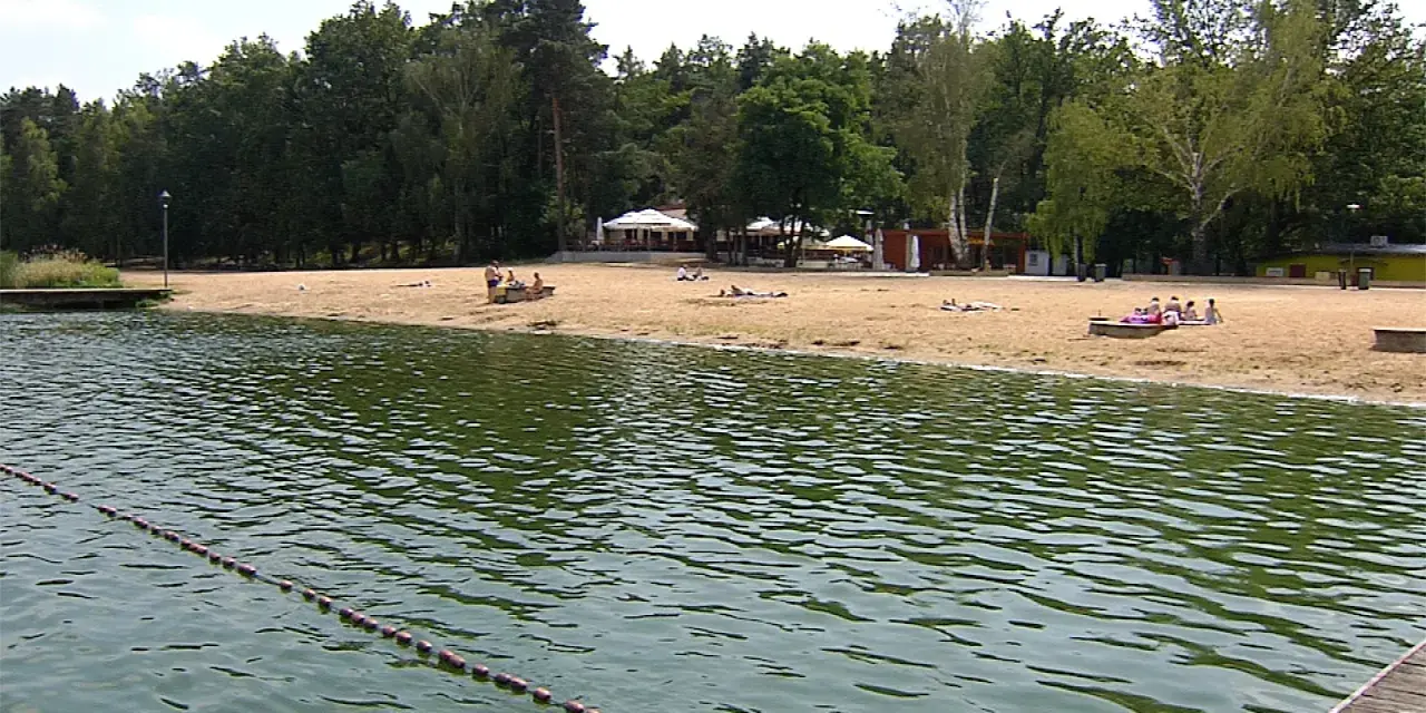 Plaża nad jeziorem Szperek, z kilkoma osobami odpoczywającymi na piasku i wodą w tle.