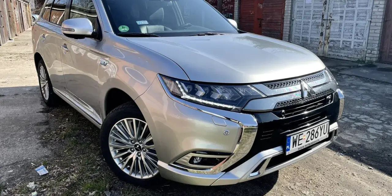 Srebrny Mitsubishi Outlander PHEV na tle garaży. Wiele osób szuka mitsubishi outlander opinie przed zakupem.