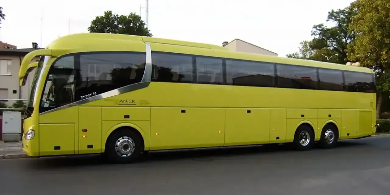 Żółty autokar firmy ANICK stoi na ulicy. Trudno określić, ile miejsc ma autokar, ale wygląda na bardzo pojemny.