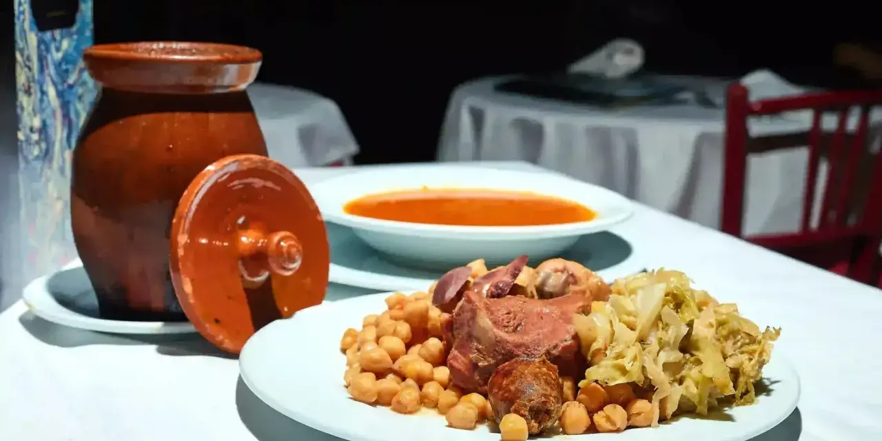 Plato de cocido madrileño con garbanzos, carne, repollo y sopa en un cuenco.