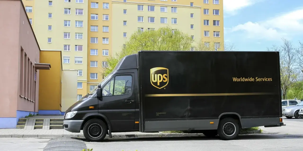 Czarny van UPS z napisem "Worldwide Services" na tle bloku mieszkalnego. Zastanawiasz się, ile zarabia kurier UPS?
