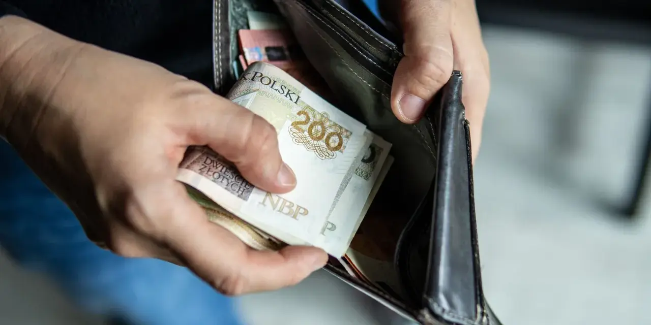 Ręce wkładają polskie banknoty 200 zł do portfela. Czy można mieć dwóch komorników na pensji, gdy pieniędzy jest tak mało?