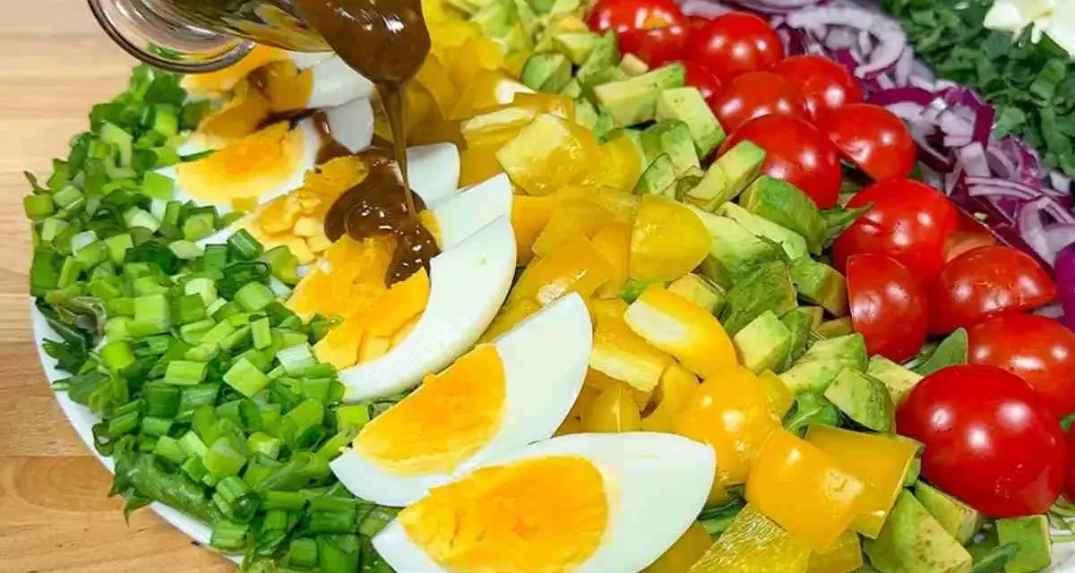 Un'insalata di avocado colorata con uova sode, pomodorini, peperoni gialli e cipolla rossa, condita con una salsa scura.