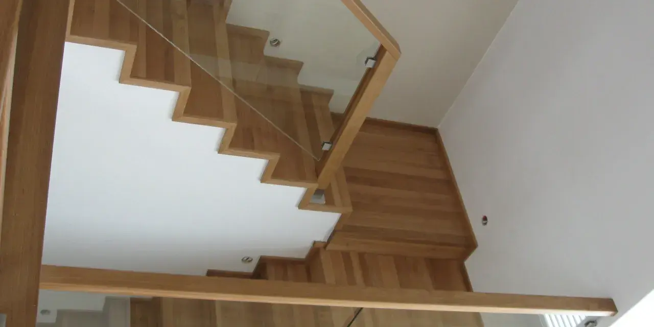 Nowoczesne schody dywanowe na beton, z drewnianymi stopniami i szklaną balustradą, tworzą lekkość i elegancję.