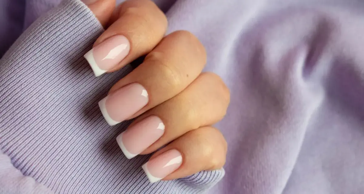 Dłoń z paznokciami w stylu french kolor, na tle lawendowej bluzy. Klasyka i elegancja.