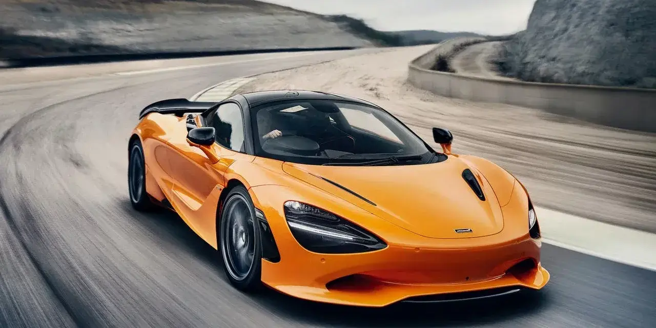 Pomarańczowy McLaren 750S z czarnym dachem sunie po torze wyścigowym, tworząc dynamiczny obraz prędkości i mocy.