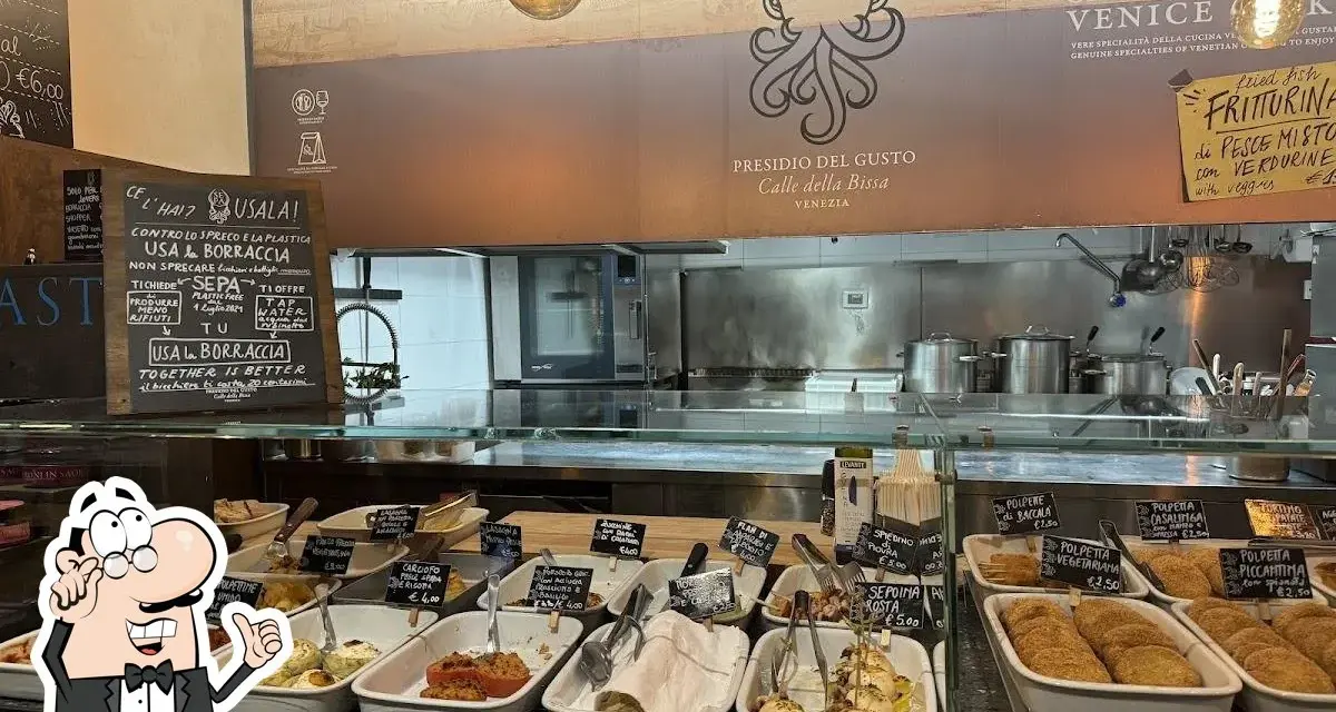 A display case filled with small dishes of food, with a chalkboard menu and a restaurant logo in the background.