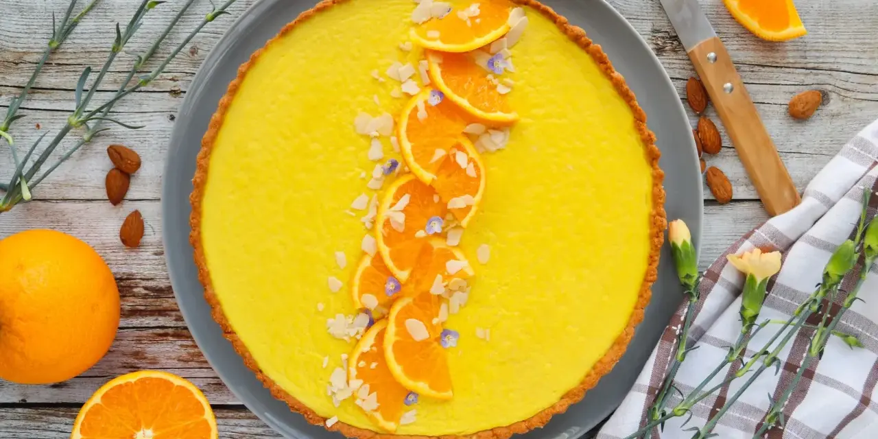 Une délicieuse tarte à l'orange, garnie de fines tranches d'orange, d'amandes effilées et de petites fleurs bleues. Un régal visuel et gustatif.