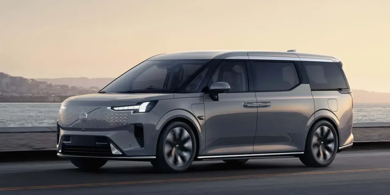 Szary luksusowy van elektryczny Volvo EM90 w ruchu drogowym nad morzem.