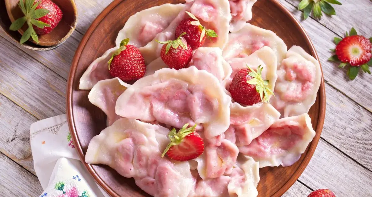 Pyszne pierogi z truskawkami, ozdobione świeżymi owocami, wyglądają apetycznie na glinianym talerzu.