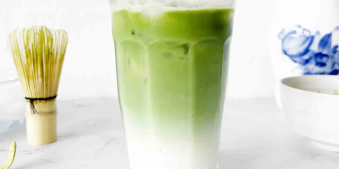 En isig matcha latte med lager av mjölk och grönt te. Bredvid står en bambuvisp, redo att blanda nästa goda dryck.