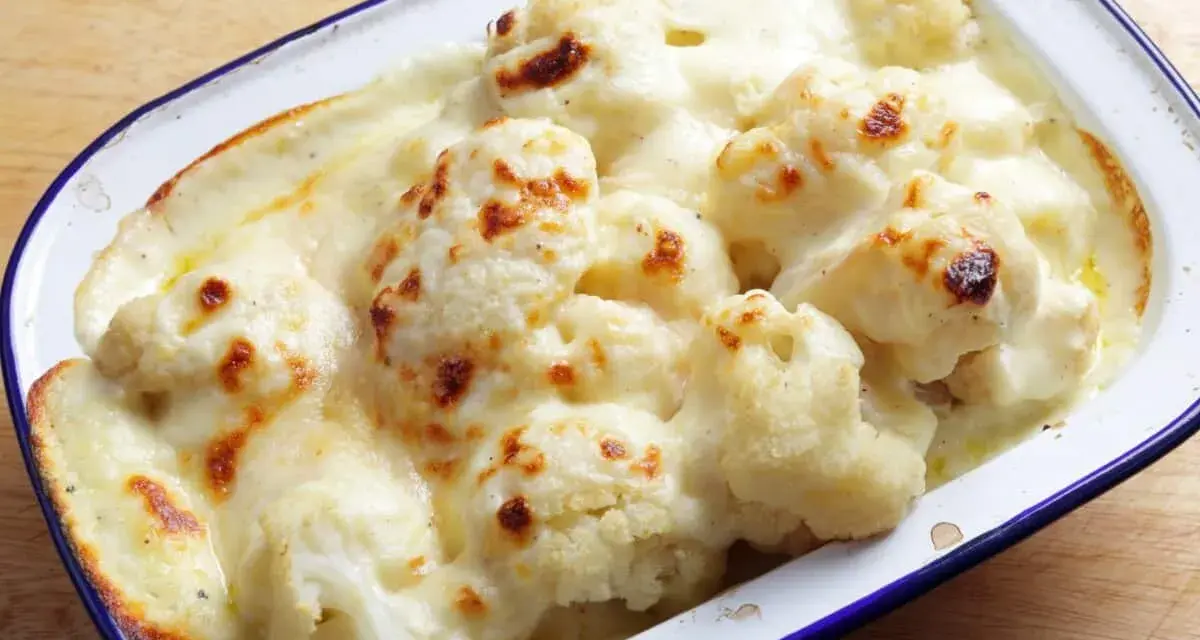 Coliflor gratinada con bechamel cremosa, dorada y burbujeante en una fuente.