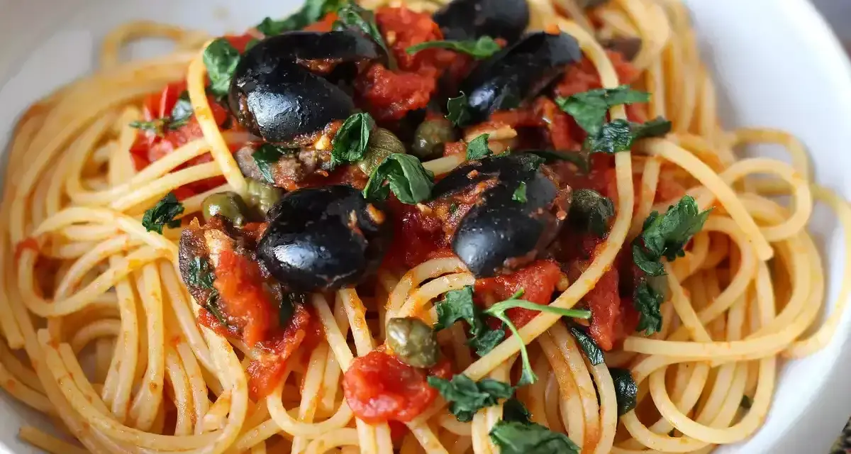 Un piatto invitante di spaghetti alla puttanesca, con olive nere, capperi e pomodoro fresco, guarnito con prezzemolo.