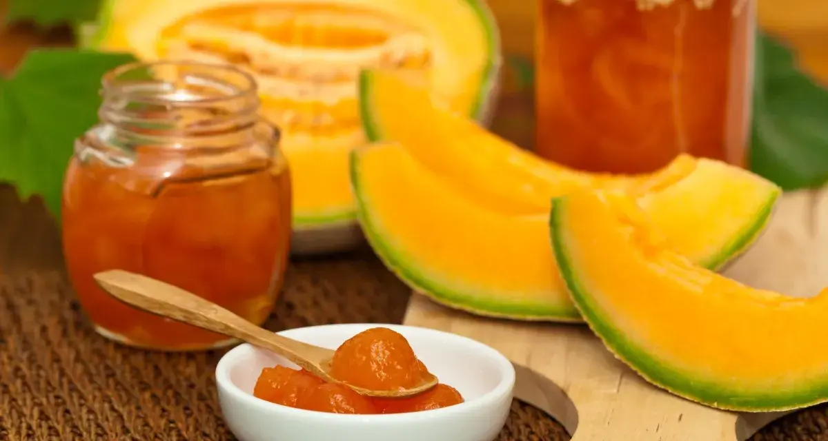 Marmellata di melone in vasetti, con fette di melone fresco e un cucchiaino pieno di confettura.