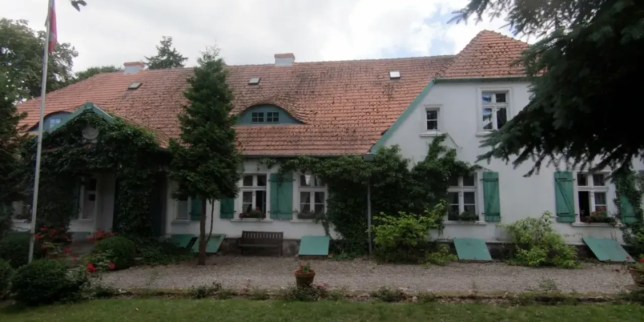 Dwór Wybickich otoczony zielenią, z charakterystycznym dachem i oknami.