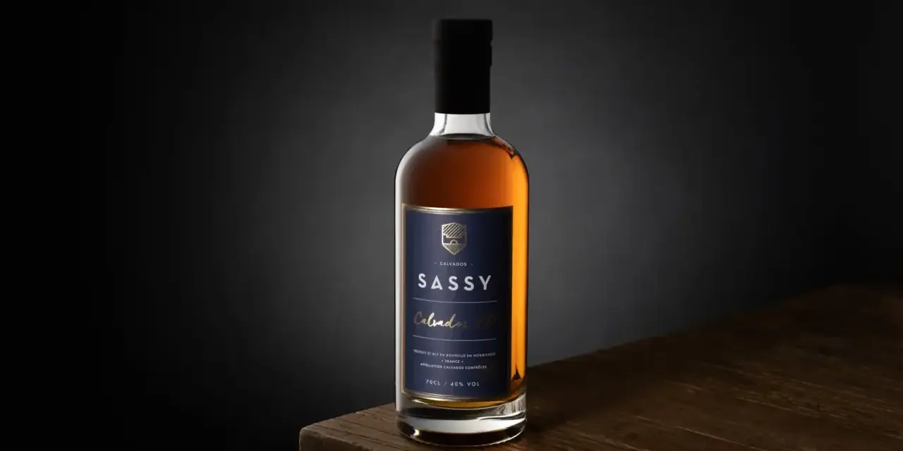 Packshot photo d'une bouteille de Calvados SASSY XO ambré, posée sur une table en bois.
