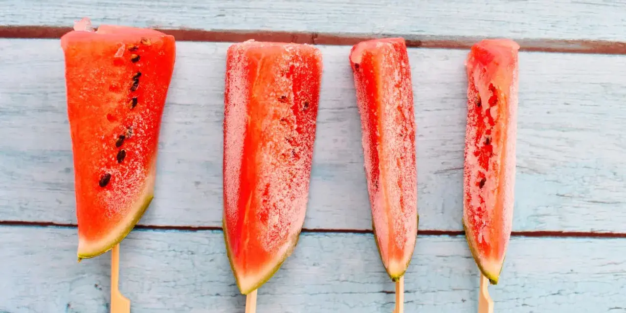 Vier gefrorene Wassermelonenstücke auf Stöcken, bereit zum Genießen. Eine erfrischende Idee für Wassermelone einfrieren.