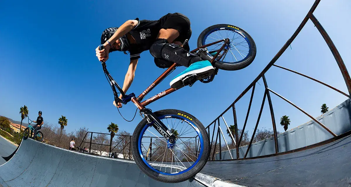 A BMX rider, possibly Chelsea Wolfe, performs a trick on a ramp against a clear blue sky.