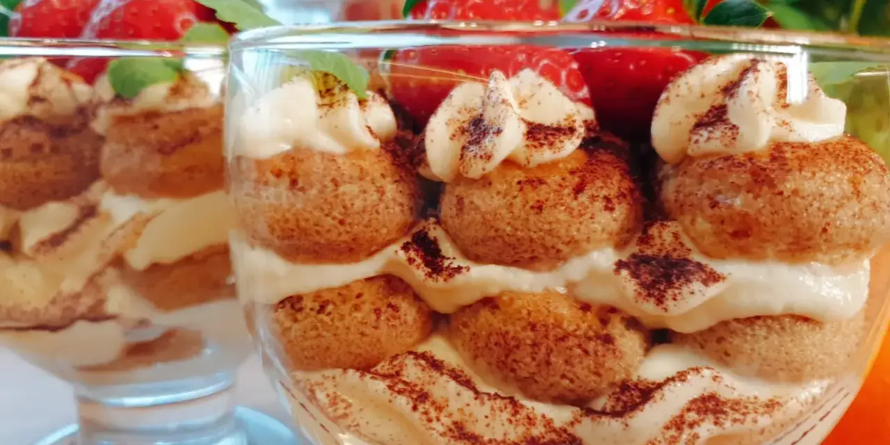 Pyszne tiramisu w pucharkach, przełożone kremem i biszkoptami, ozdobione truskawkami i kakao.